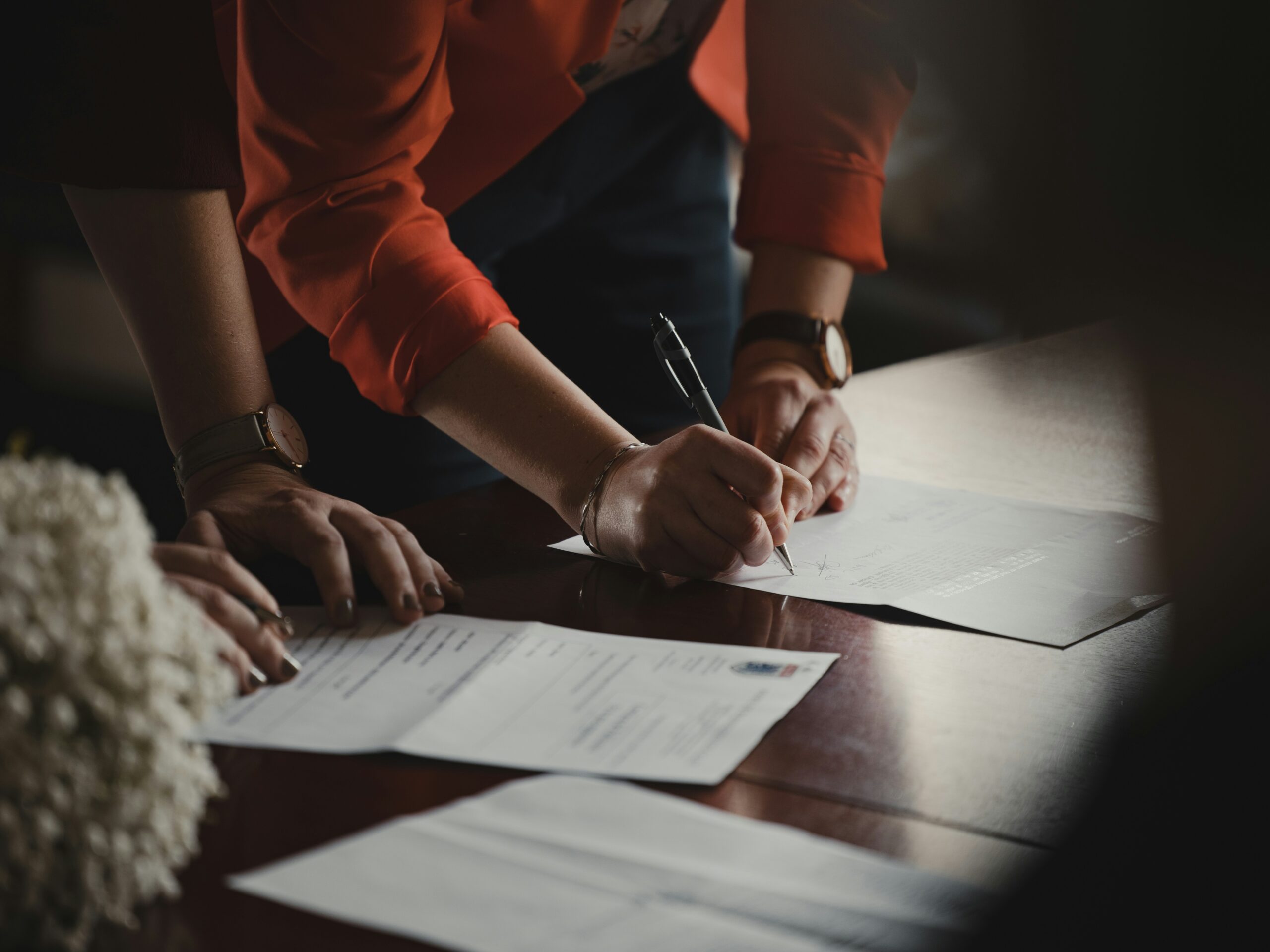 Two people signing estate paperwork at a wooden desk